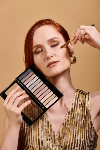 Redhead woman applying eye shadow  and holding palette on beige background, beauty advertisement — Stock Photo