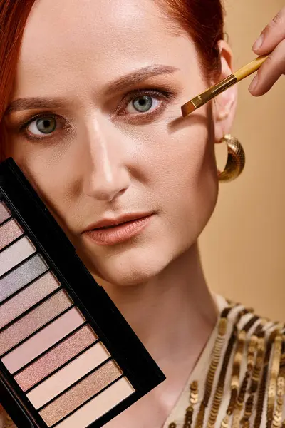 Close up de mulher ruiva aplicando sombra nos olhos e segurando paleta no fundo bege, cor pastel — Fotografia de Stock