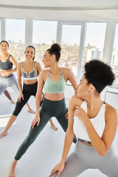 Groupe de femmes joyeuses et diversifiées en vêtements de sport pratiquant pilates avec entraîneur afro-américain féminin — Photo de stock
