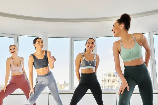 Groupe de femmes heureuses et diversifiées en leggings et crop tops pratiquant pilates ensemble en studio — Photo de stock