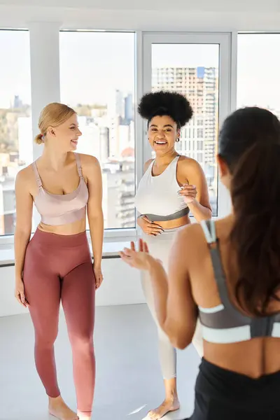 Feminino pilates treinador falando com feliz mulher multiétnica em sportswear antes da aula, esporte — Fotografia de Stock