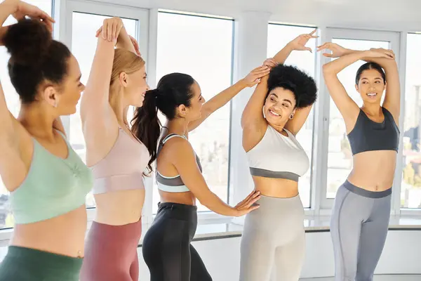 Happy pilates instructor helping african american woman with stretching exercise near sportswomen — Stock Photo