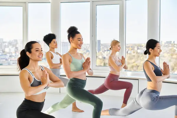 Gruppe fröhlicher multikultureller Frauen beim Ausfallschritt mit betenden Händen, während sie Pilates praktizieren — Stockfoto