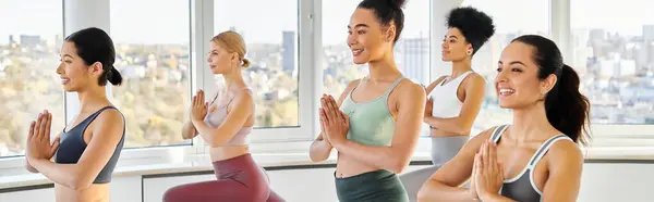 Banner of happy multicultural women doing lunges with praying hands while practicing pilates — Stock Photo