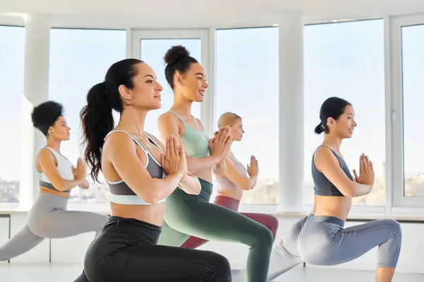 Group of happy multicultural women doing lunges with praying hands while practicing pilates — Stock Photo