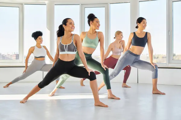 Groupe de femmes interraciales heureux faisant des fentes tout en pratiquant pilates ensemble dans le studio de bien-être — Photo de stock