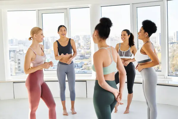 Groupe de cinq femmes multiculturelles heureuses debout dans les vêtements de sport et bavarder devant pilates classe — Photo de stock