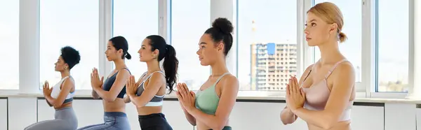 Bannière de cinq jeunes femmes multiculturelles avec des mains priantes pratiquant le yoga dans un studio lumineux — Photo de stock