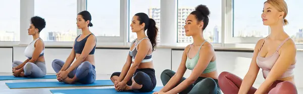 Grupo de mujeres descalzas y jóvenes interracial meditando mientras practican yoga sobre esteras, pancartas - foto de stock