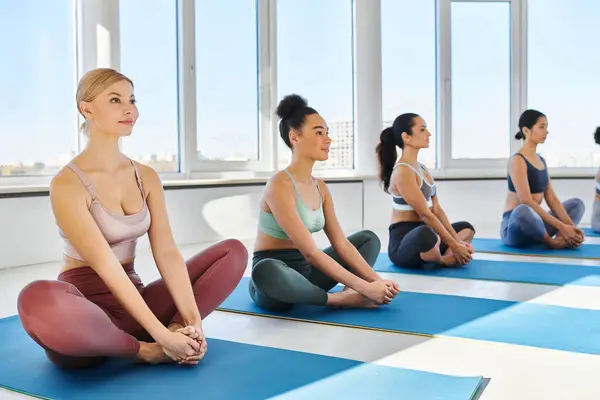 Grupo de mujeres descalzas y jóvenes multiculturales meditando mientras practican yoga sobre esterillas en estudio - foto de stock