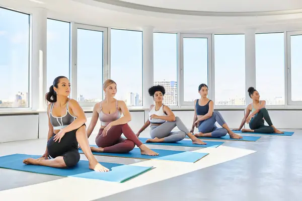 Group of barefoot and young multicultural women sitting in half lord of the fishes yoga pose on mats — Stock Photo