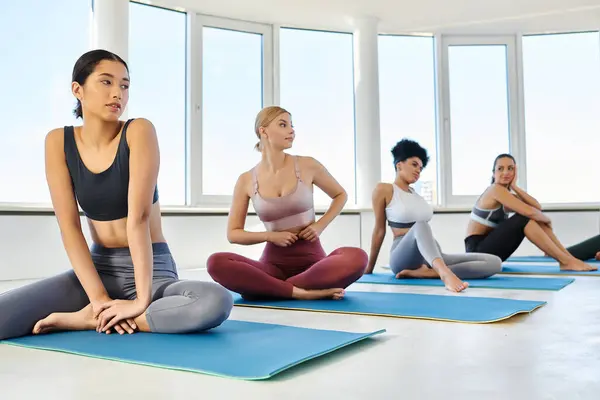 Joven asiático mujer en sportswear sentado en mat al lado de multicultural amigos durante yoga clase - foto de stock