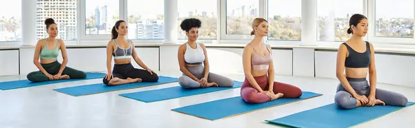 Cinco mujeres descalzas y jóvenes multiculturales meditando mientras están sentadas en la pose de loto de yoga, pancarta - foto de stock