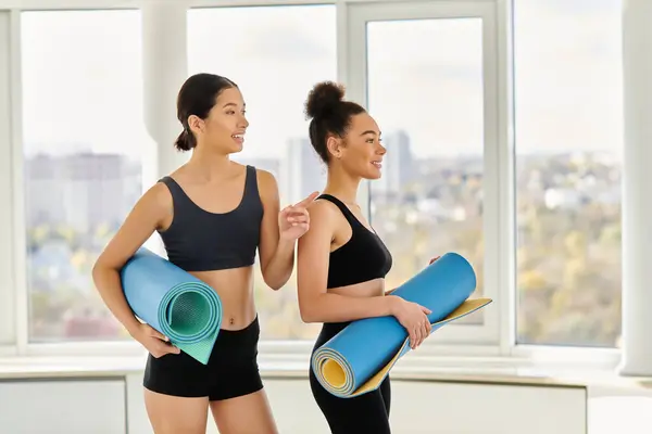 Mulheres multiculturais e jovens felizes em seus 20 anos de pé com tapetes de ioga em estúdio, pós-treino — Fotografia de Stock