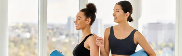 Happy multicultural young women in their 20s standing with yoga mats in studio, post-workout banner — Stock Photo