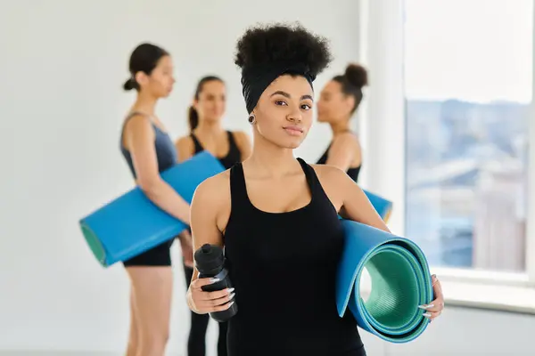 Focus on african american woman standing with fitness mat and sports bottle in yoga studio — Stock Photo