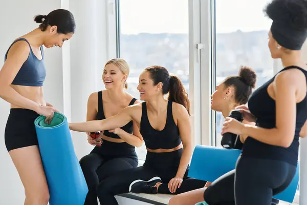 Cheerful interracial young women in 20s chatting while sitting next to window in pilates studio — Stock Photo