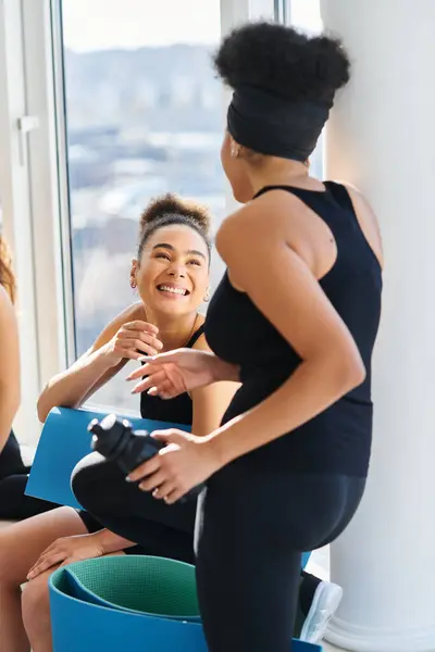 Two african american women in sportswear chatting while resting after workout in pilates studio — Stock Photo