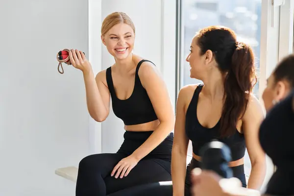 Happy blonde woman with jumping rope laughing while chatting with her friend in pilates studio — Stock Photo