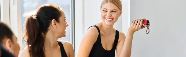 Mujer rubia feliz con saltar la cuerda riendo mientras charla con un amigo en el estudio de pilates, pancarta - foto de stock