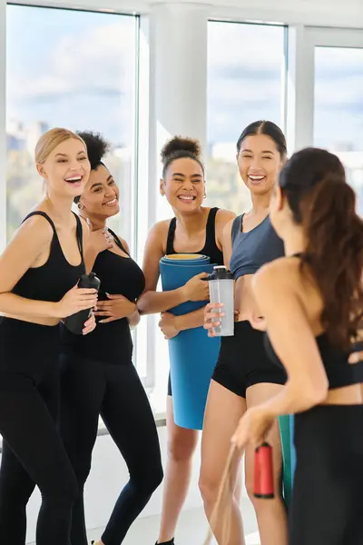 Cinco jóvenes mujeres multiculturales en activo desgaste charlando y riendo después del entrenamiento en el estudio de pilates - foto de stock
