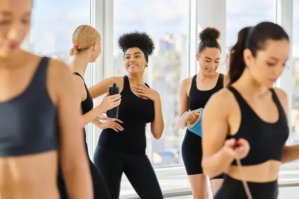 Cinco jóvenes mujeres multiculturales en activo desgaste charlando y sonriendo después del entrenamiento en el estudio de pilates - foto de stock