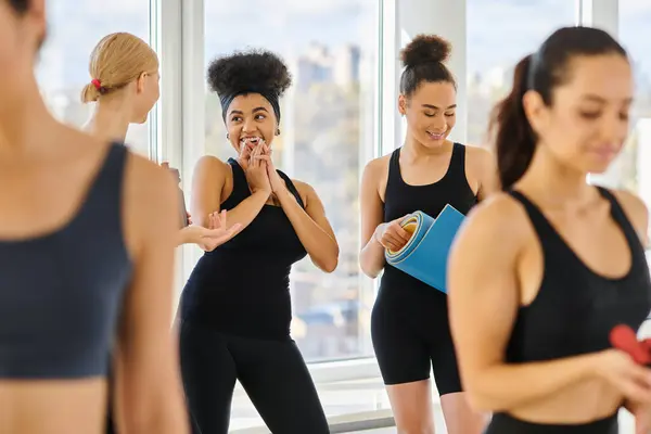 Cinco mujeres felices y jóvenes multiculturales en activo desgaste charlando después del entrenamiento en el estudio de pilates - foto de stock