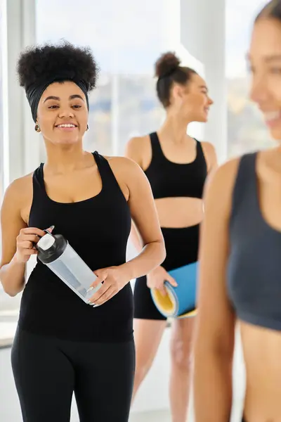 Centrarse en la mujer afroamericana feliz mirando a sus amigos borrosos después del entrenamiento en el estudio de pilates - foto de stock