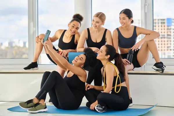 Groupe de cinq et joyeuses femmes multiculturelles en vêtements de sport prendre selfie après le cours de yoga — Photo de stock
