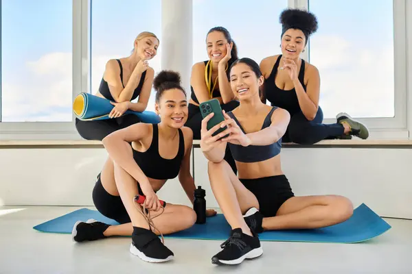 Group of five and cheerful interracial female friends in sportswear taking selfie after yoga class — Stock Photo