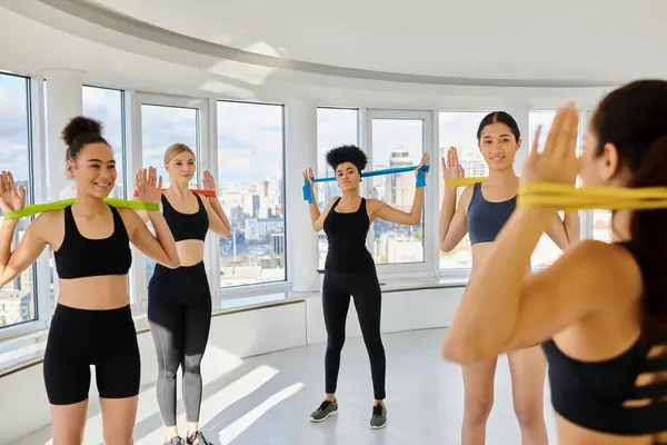 Group of happy diverse women in sportswear looking at trainer while exercising with resistance bands — Stock Photo