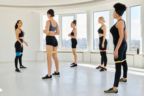 Group of diverse women in sportswear looking at trainer and exercising with resistance bands — Stock Photo
