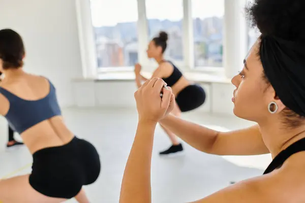Focus on african american woman exercising next to blurred sportswomen during pilates class — Stock Photo
