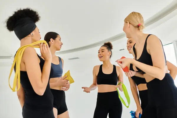 Группа счастливых разнообразных спортсменок, держащих полосы сопротивления и общающихся после тренировки пилатеса — стоковое фото