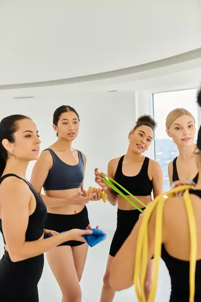 Group of focused diverse sportswomen holding resistance bands and chatting after pilates workout — Stock Photo