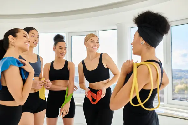 Group of positive diverse sportswomen holding resistance bands and chatting after pilates workout — Stock Photo