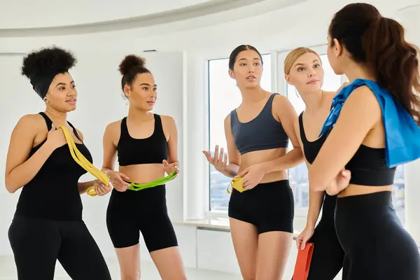 Group of motivated diverse sportswomen holding resistance bands and chatting after pilates workout — Stock Photo