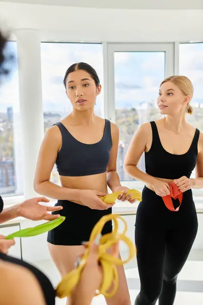 Giovane donna asiatica in piedi accanto a bionde amiche di sesso femminile e chattare post allenamento in pilates studio — Foto stock