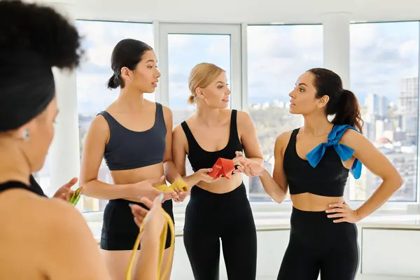 Group of motivated and serious sportswomen holding resistance bands and chatting after pilates class — Stock Photo