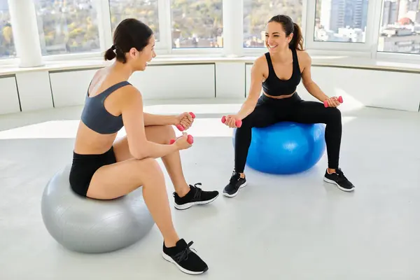Alegres y diversas amigas haciendo ejercicio con pesas en las bolas de fitness durante la clase de pilates - foto de stock