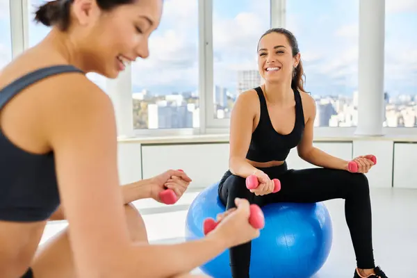 Heureux interracial femmes amis exercice avec haltères sur des balles de fitness pendant pilates classe — Photo de stock