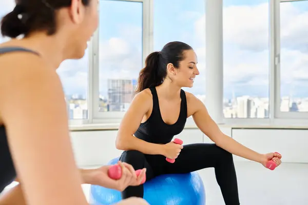 Felices amigas multiculturales haciendo ejercicio con pesas en las bolas de fitness durante la clase de pilates - foto de stock