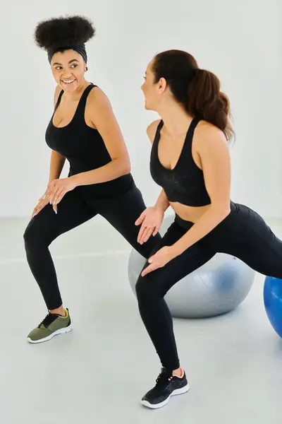 Deux amies heureuses et diverses faisant de l'exercice sur des balles de fitness pendant le cours de pilates, motivation — Photo de stock