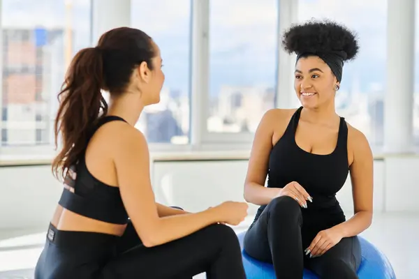 Happy and diverse female friends sitting on fitness balls and smiling during pilates class — Stock Photo