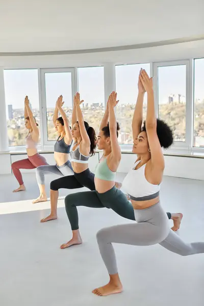 Grupo de jóvenes cinco mujeres multiculturales en ropa deportiva practicando yoga juntas en estudio - foto de stock