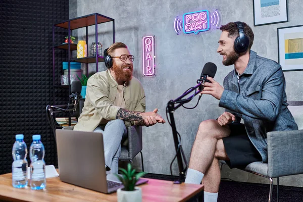 Entrevistador guapo barbudo y su invitado con auriculares en el estudio discutiendo preguntas, podcast - foto de stock