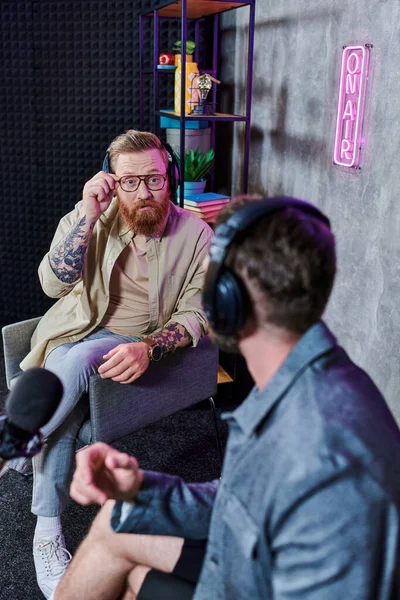 Schöner Interviewer mit roten Haaren und sein Gast mit Kopfhörern, der Fragen diskutiert, Podcast — Stockfoto