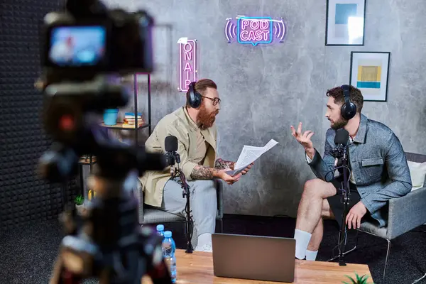 Zwei gutaussehende bärtige Männer in lässiger Kleidung mit Kopfhörern, die sich während eines Podcasts aktiv unterhalten — Stockfoto