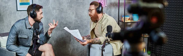 Two handsome bearded men in casual attires with headphones talking actively during podcast, banner — Stock Photo
