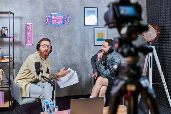 Bom olhar entrevistador elegante falando com seu jovem convidado com fones de ouvido durante podcast — Fotografia de Stock